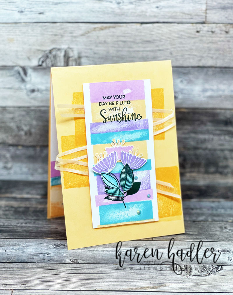 Celebrate with Flowers with Water Colour Shapes Stamp sets. The card is on a Pale Papaya Base with 3 rectangles stamped in Pale Papaya on the front. There is a sheer ribbon in the same colour going accross the card 3 times. In the middle of the card is a white strip with alternating blocks of colour running down it. The sentiment stamped in green at the top says May your Day be Filled with Sunshine. at the bottom is some leaves and 3 flowers that have been fussy cut out.