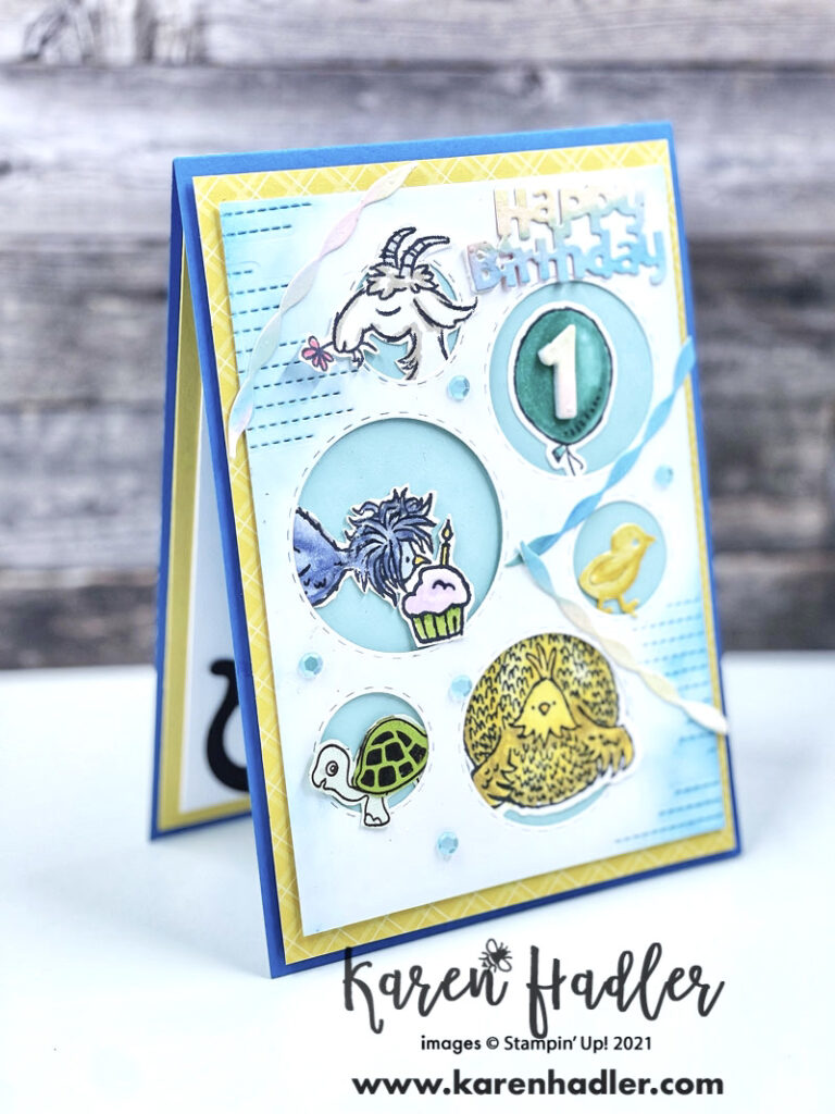 Picture this Fun Animal 1st Birthday Card. The card is on a bright blue base with a yellow mat. On top is a white mat with different size holes. In these holes are different animals a turtle, chickens, chicks, a goat. There are also streamers and the words Happy Birthday have been die cut out. It is a bright happy Card.