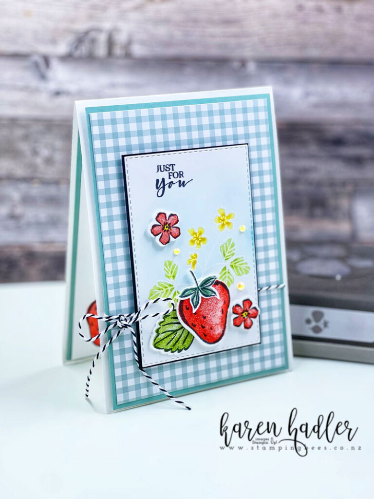 Sweet Strawberries Just for You is on a White card base with Soft Succulent mats. The top layer is Gingham paper with a smaller white rectangle matted with black on top. This is is white embossed with flowers and leaves that have ben coloured green and yellow. On top is a single red strawberry with a large green leaf and two smaller red flowers. There is black and white twine tied in a bow. 