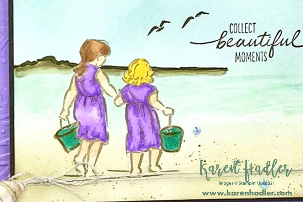 A closer look at Collect Beautiful Moments by the Seaside. A sand coloured card base with a soft purple mat. On the front is a scene on the beach with two girls holding hands walking towards the water.They each have a green bucket. The sentiment reads Collect beautiful moments