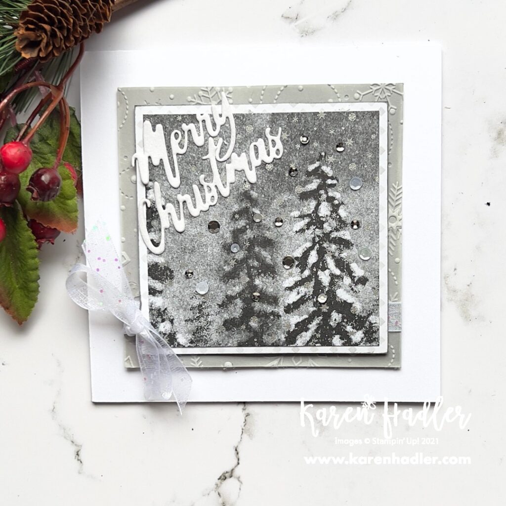 A picture of a card the is Black, White, Gray and silver. The picture is some wintery trees with snow. The words are cut out in White and say Merry Christmas. There is also a White glittery bow on the left.