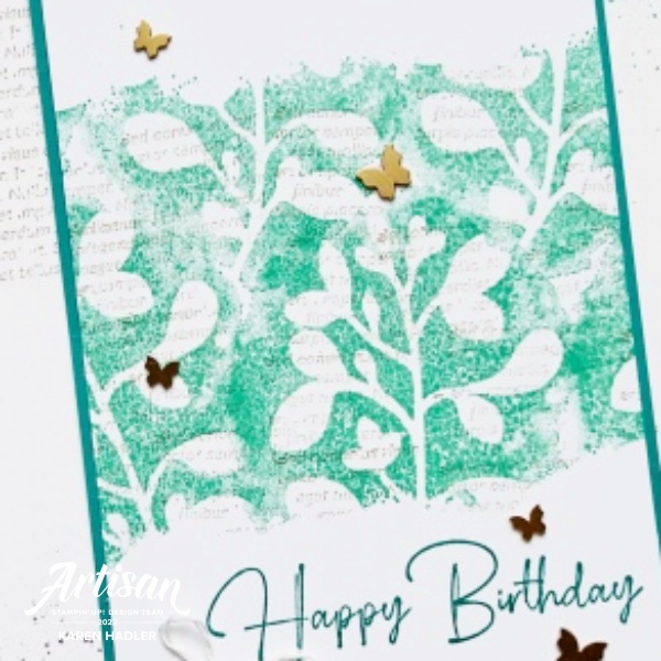 A close up look atA picture of a card with Text. The card is standing and is white and teal. In the centre is a stamped area with white leaves. The words say Happy Birthday and there are small butterflies.