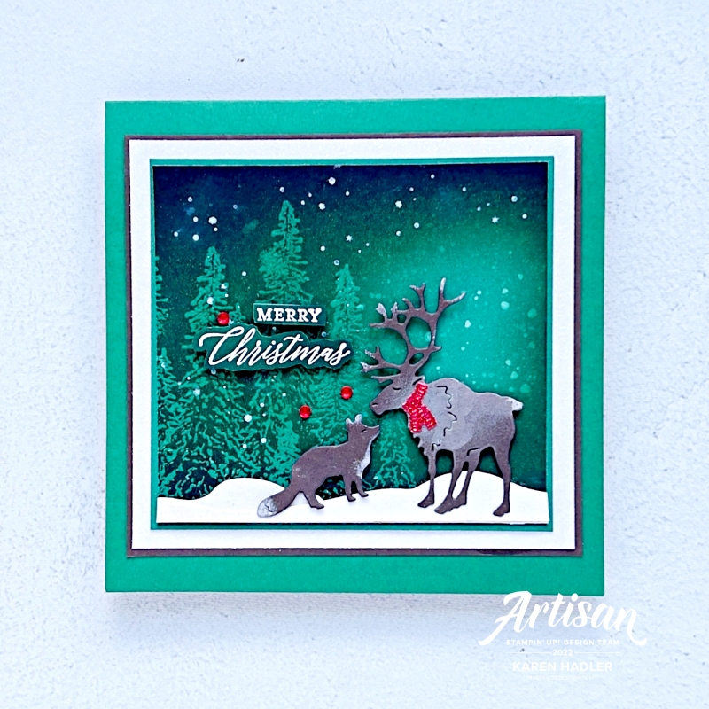 A picture of a green square greeting card with a nighttime starry sky blended background and a Reindeer and a Fox kissing. The sentiment reads Merry Christmas.