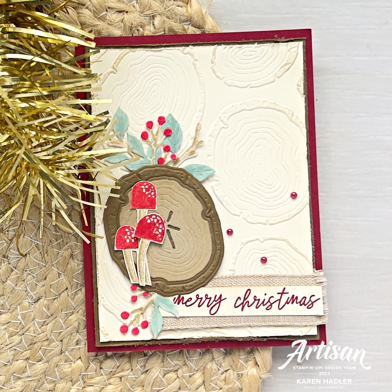 A picture of a Christmas Card with lots of wood texture and Rings. The colours are reds and browns with berries and Toadstools. The sentiment reads Merry Christmas