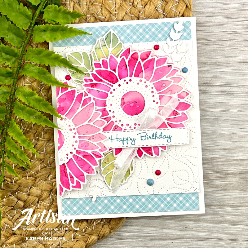 A picture of a Birthday Card with two bright pink water coloured Sunflowers with a white and blue Gingham background.