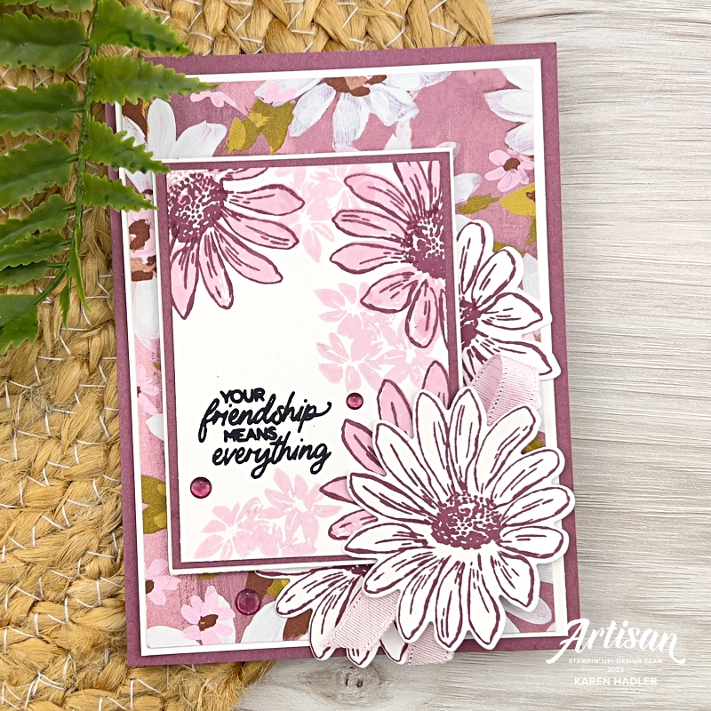 A greeting card on a Moody Mauve base with pink and whoiDaisies all over the front. There is a White rectangle with some stamped pink daisies on it and amongst them is the stamped sentiment Your friendship means everything. There are also 3 large white daisies to the bottom right.