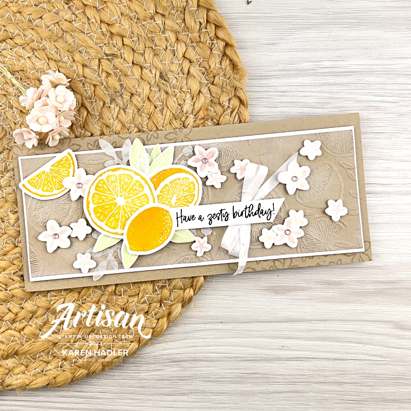 A greeting card in Crumb cake embossed with lemons. There are small white and pink flowers scattered . To the left is some yellow Lemons and leavesThe sentiment reads have a Zesty Birthday.