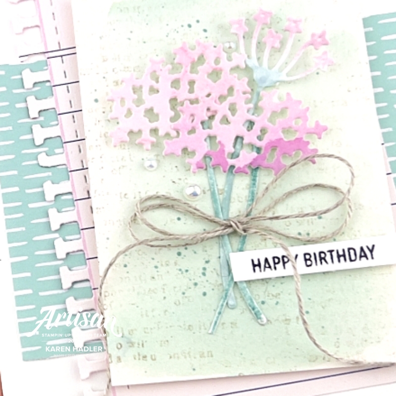 A close up of A picture of a greeting card in the centre is a water coloured piece of card in Pool Part on top of this is  pink water coloured flowers that look a little like hydrangeas. the sentiment reads Happy Birthday and there is a large double linen thread bow.The background has a piece of co-ordinating Pool party paper with small white lines. On top of this is a pice of paper that looks like it is torn from a notebook.