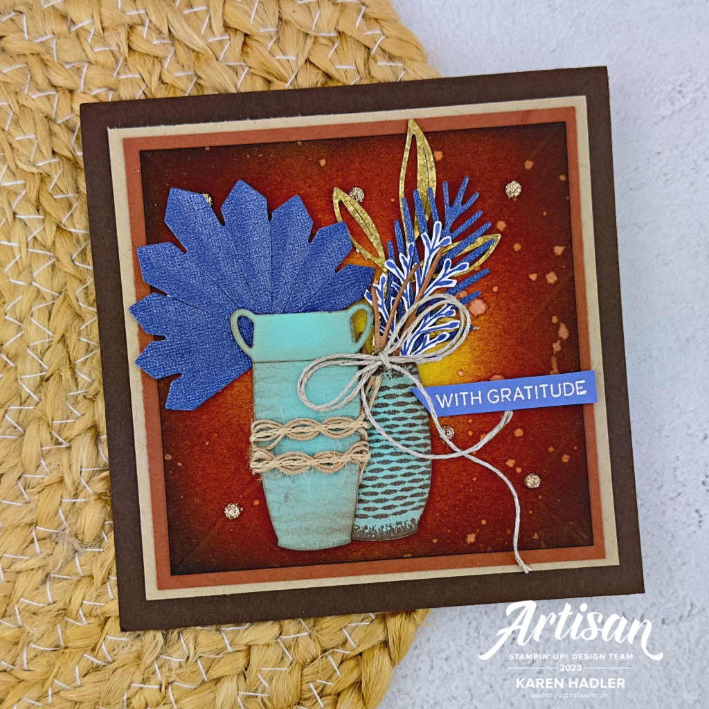 A picture of a greeting card that has a dark moody brown background with water splattered on in droplets. In the foreground are two pool party vases with blue and gold leaves and palms. The sentiment reads with Gratitude