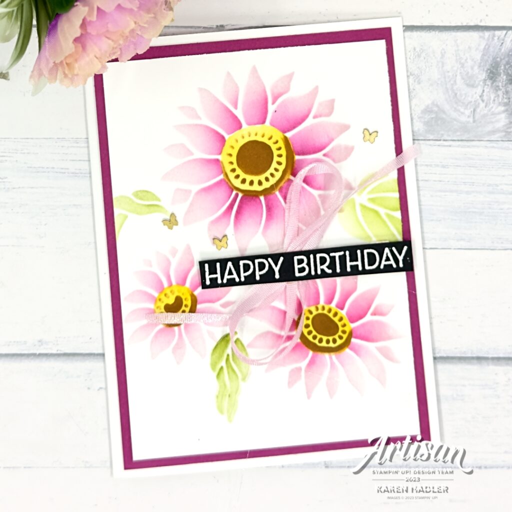 A greeting card on a white card base with a Berry Burst mat The front has another white mat with 3 gorgeous pink flowers with yellow and brown centres. There are 3 green leaves and the sentiment Happy Birthday is White embossed on black cardstock. This is across the flowers with a pink bow underneath. The are also 3 brass butterflies on the card.