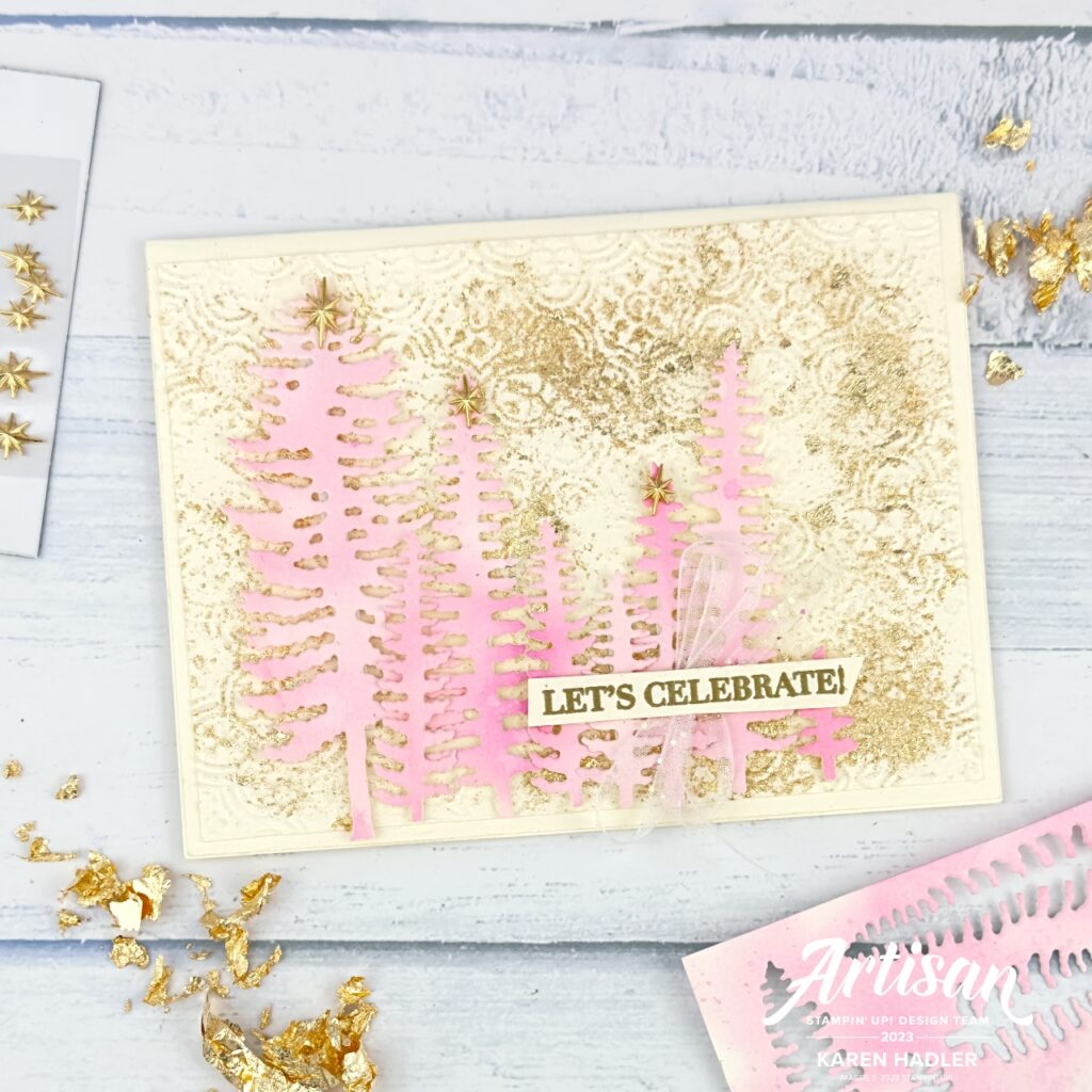 A greeting card that reads let celebrate. The background is embossed with a distressed Tile embossing folder and there is gilded leafing randomly placed. on top is a row of pink water coloured trees . The sentiment is gold embossed across the top of the trees and underneath is a small iridescent bow.