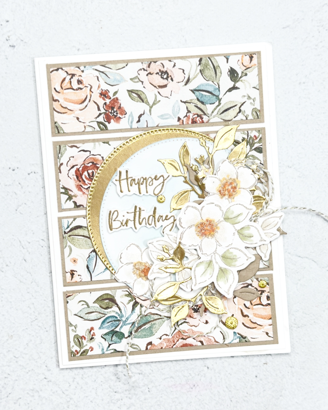 A floral Birthday card on a white base. With Gold and sparkle. There is a gold and white circle in the middle with a posy of flowers on the right hand side . The sentiment is gold embossed inside this circle and which also has gold leaves.