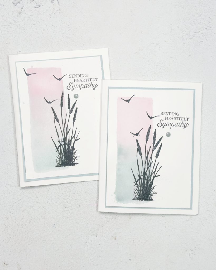 Two white based cards with a faux water colour rectangle shape going down the left hand side of pink and blue.. Stamped on on top of this is grasses in black and 3 birds in the sky. The sentiment is towards the top right and reads Sending Heartfelt Sympathy.