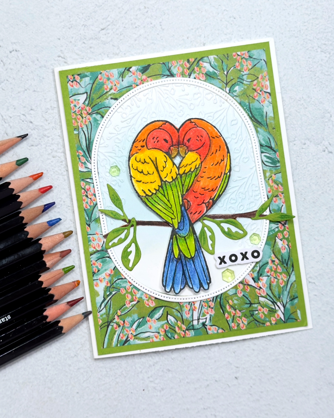 A greeting card send love and hugs with two gorgeous bright blue green,yellow red and orange parakeets giving each other a cuddle.