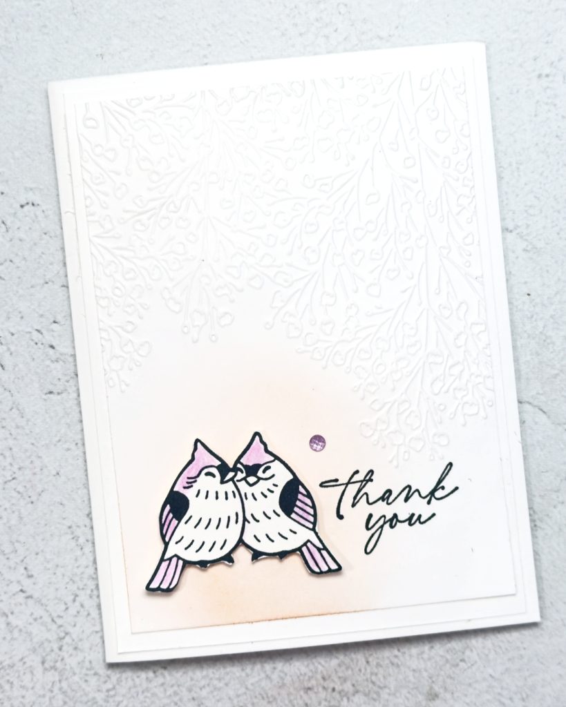 A white greeting card that says thank you. In the bottom left is two birds with white stomachs and purple wings snuggling up together.