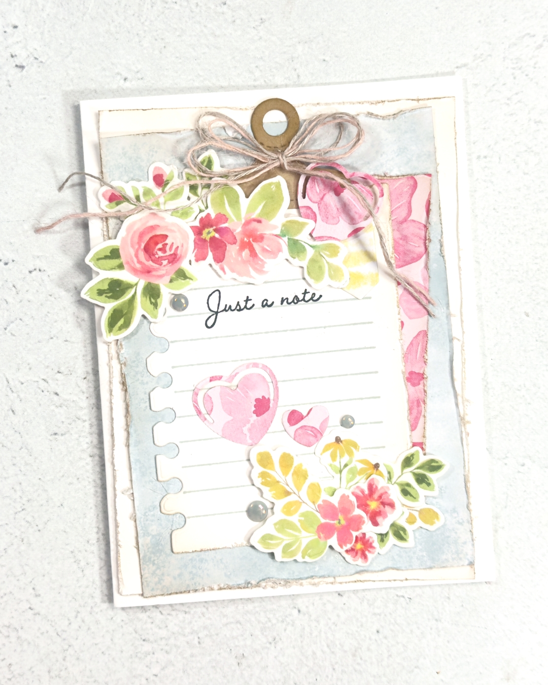 A greeting card that has layers of soft pastel blues and pinks. There is a note card in the middle that has the words just a note stamped in the middle.
