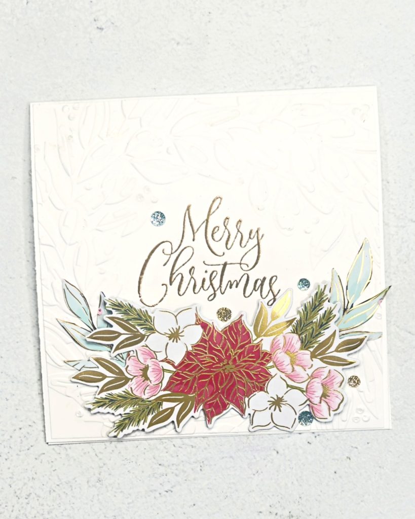 A square white christmas card with a poinsettia in the middle with leaves and flowers on either side and stamped in a half circle above is the sentiment Merry Christmas.