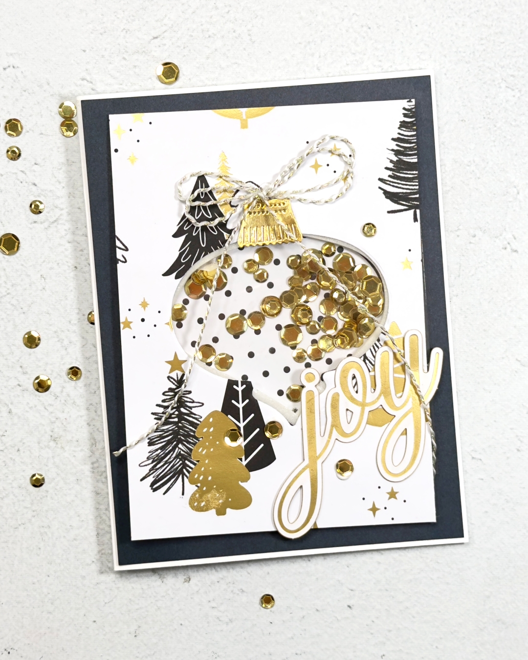 A Black Gold a White Christmas Shaker card. The shaker is inside a large ornament with gold sequins the sentiments in large gold lettering reads Joy