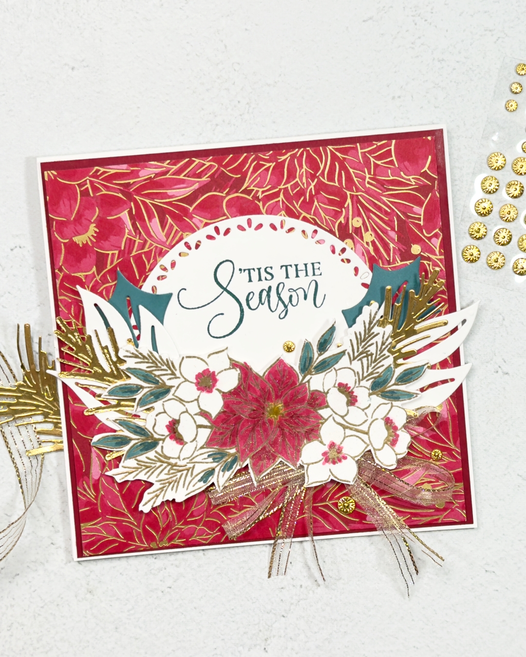 A square Christmas Card with red green and gold colours. There is a poinsettia in the middle with leaves and flowers on either side and stamped in a half circle above is the sentiment Tis the Season.