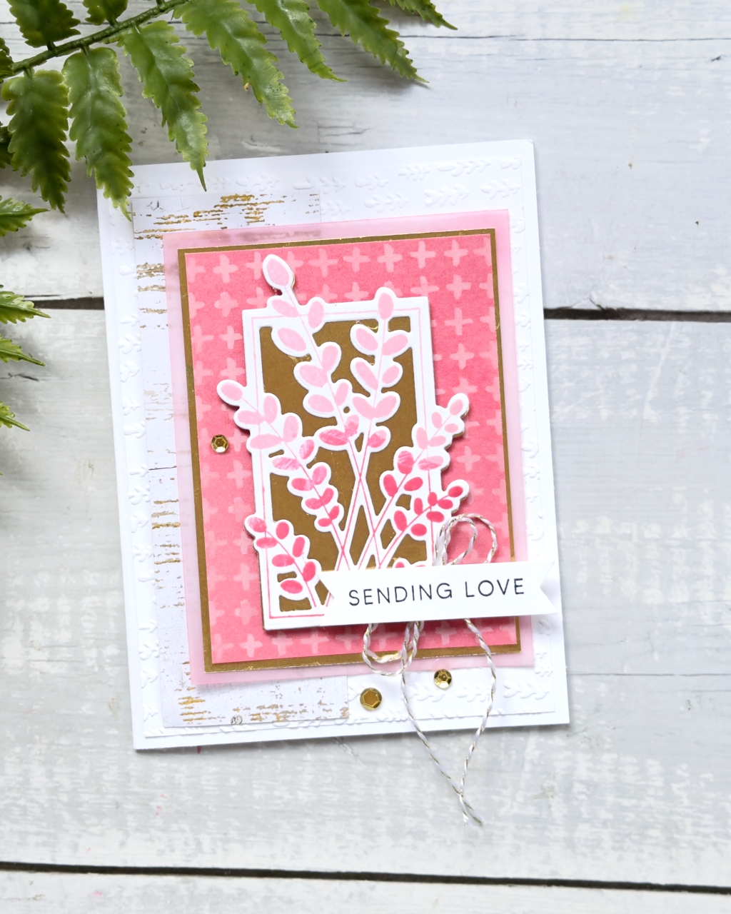 A greeting card with the sentiment Sending Love the colours are pink and strawberry on a white background. In the centre are some pink leaves . There is gold matting and embellishments