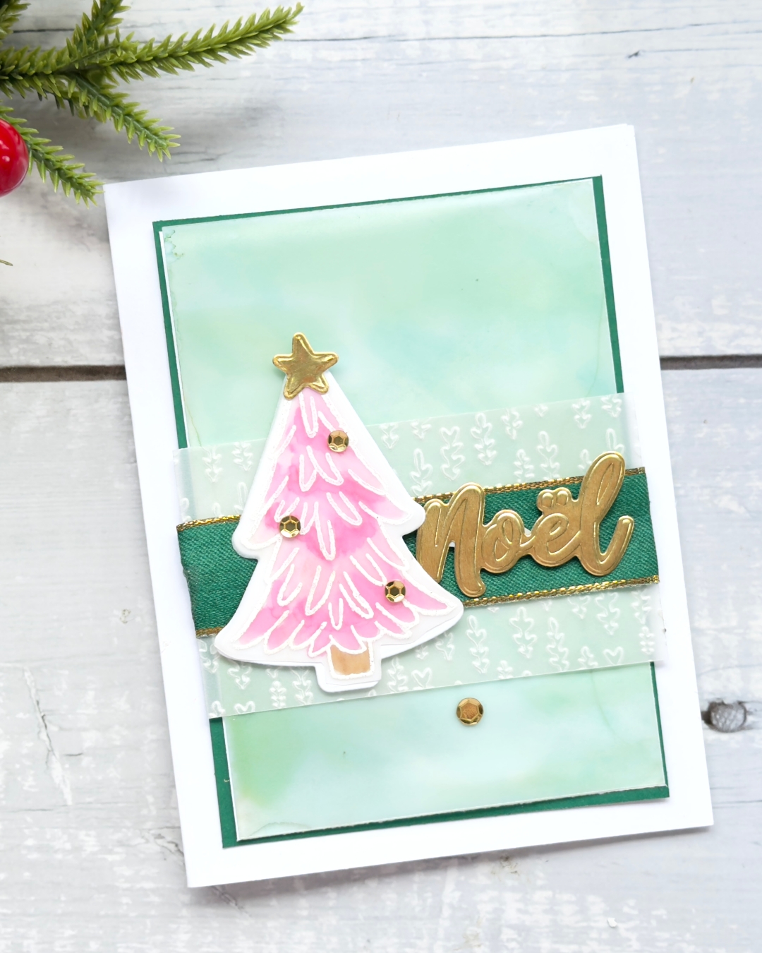 A christmas card with a green background a pink Christmas tree and a gold sentiment that reads Noel.