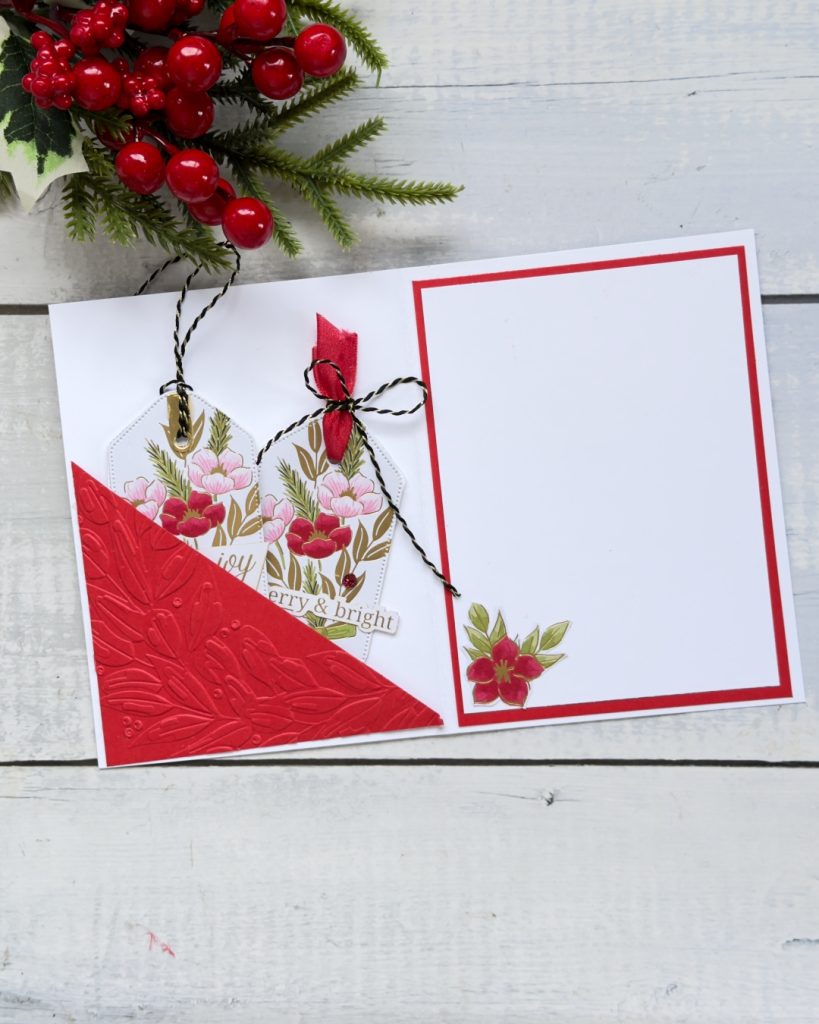 The inside of a white and red card. on the left is a small red pocket with 2 tags. these tags have red and pink and gold flowers with black and gold twine coming from the top. The sentiment reads merry & Bright