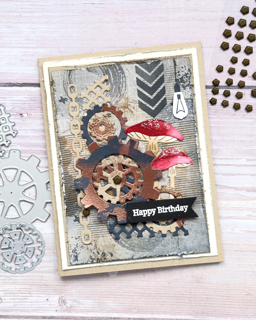 A masculine birthday  card in browns and blacks with circle stripes dots cogs and lots of layers. There is also to red toadstools and a light bulb hanging from the top of the card.