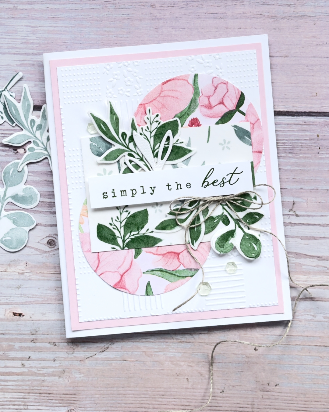 Stampin’ Up! handmade card using floral patterned paper, layered greenery die cuts, embossed white cardstock, linen thread bow, and a “simply the best” sentiment in soft pink and green tones.
