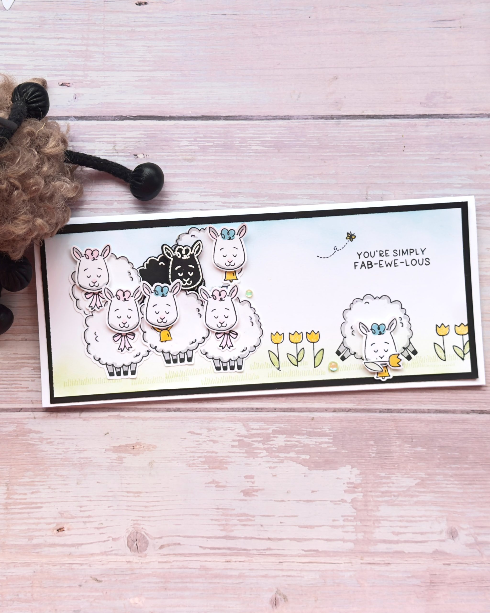 Slimline handmade card created with the Stampin’ Up Woolly Friends bundle, featuring a flock of stamped and punched sheep, including a black sheep, soft ink-blended grass, yellow tulip flowers, and the sentiment “You’re Simply Fab-Ewe-Lous.”