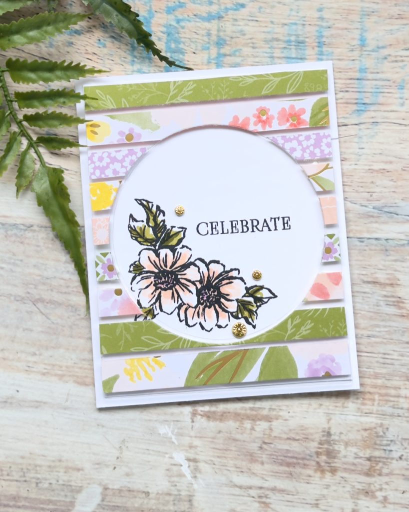 Handmade floating technique card with floral designer paper strips, circular opening and stamped flowers with Celebrate sentiment and gold embellishments.