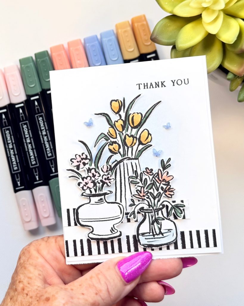 Handmade thank you card featuring layered black and white sketched vases with soft colouring in Stampin’ Up! 2026–2028 In Colours, accented with striped designer paper and small blue embellishments.