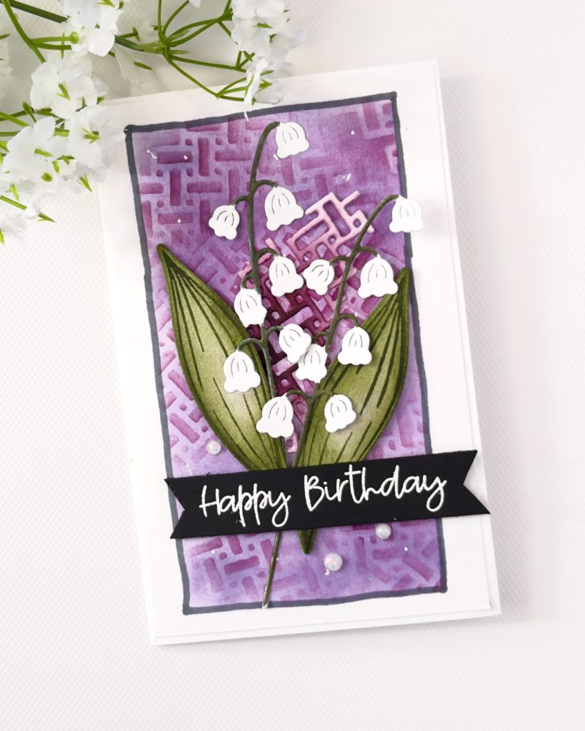 Handmade birthday card with lily of the valley die cuts on a purple textured background, layered leaves, trellis detail, and black Happy Birthday sentiment.