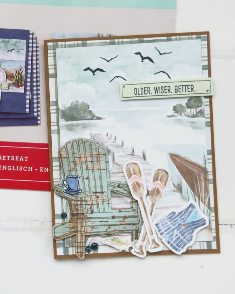 Handmade masculine birthday card created with the Lakeside Retreat Paper Pumpkin Kit featuring a peaceful dock and lake scene with Adirondack chair, paddles, life jacket embellishments, birds in the sky, and “Older. Wiser. Better.” sentiment.